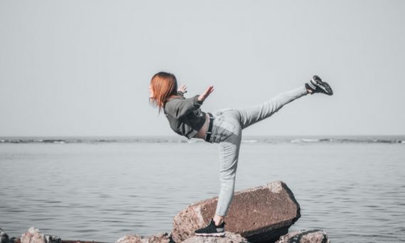 A woman in denim balances on rocks by the ocean, showcasing outdoor adventure and freedom.